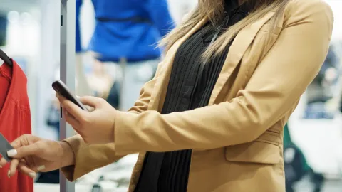 Nainen skannaa älypuhelimellaan vaatteen hintalapun