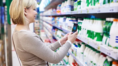 Nainen skannaa älypuhelimellaan tuotepaketin koodin